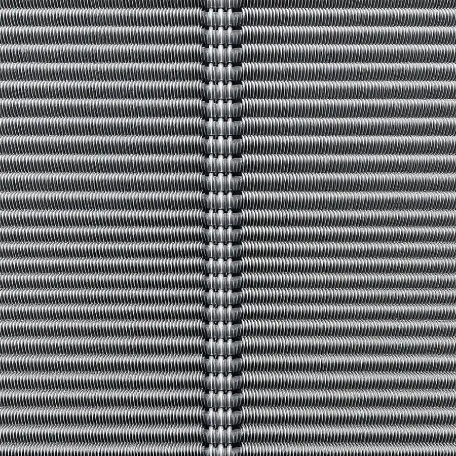 Close-up of the flat face of an evaporator coil with dense vertical aluminium fins and copper tube bends along one edge