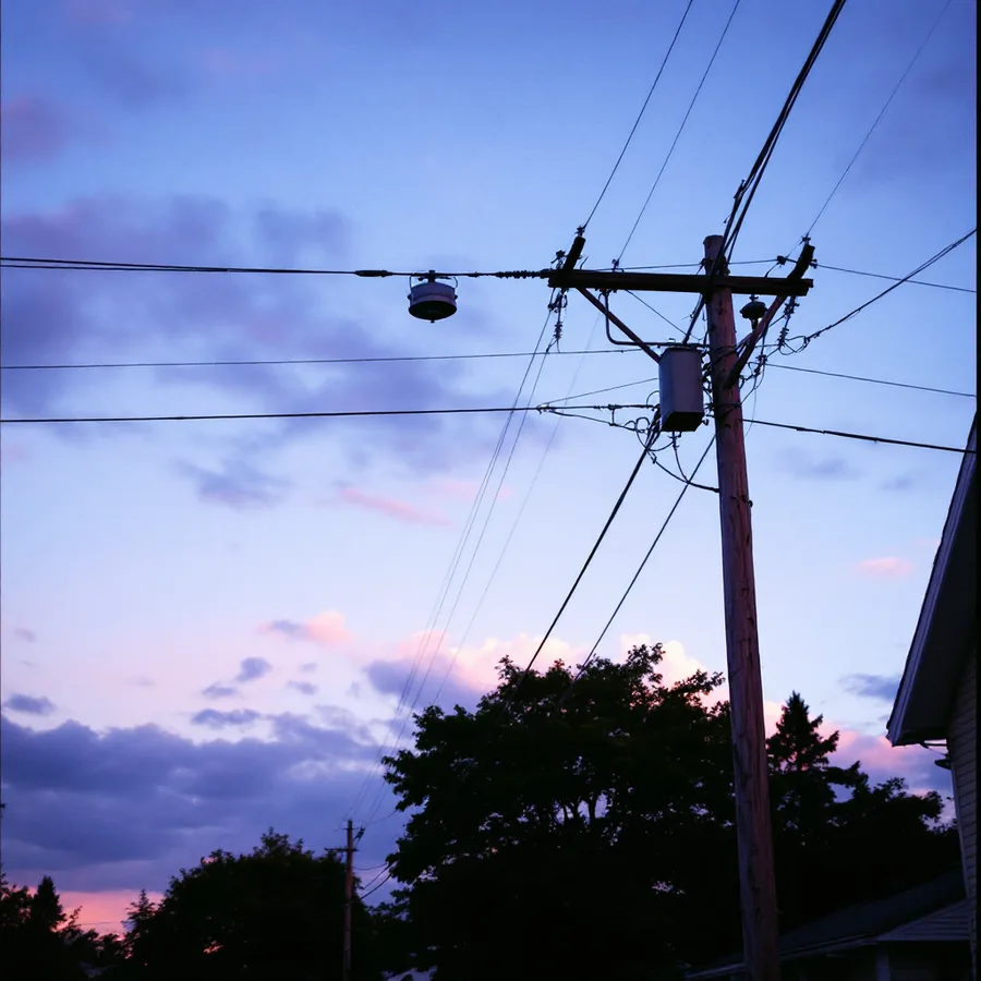 Residential electrical distribution lines and a wooden utility pole with transformers against an evening sky above a suburban street
